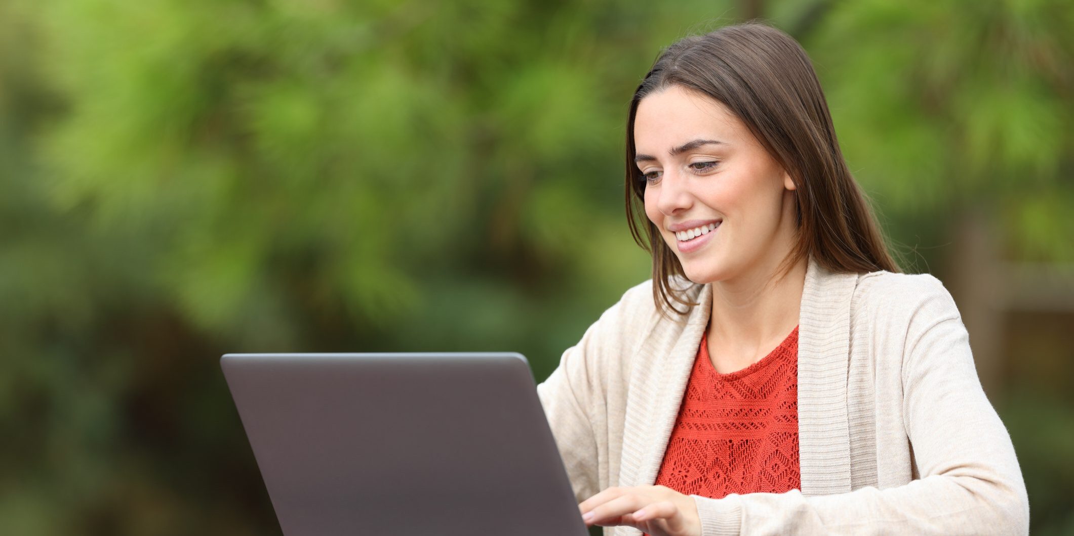 Happy woman using laptop sitting in a park table